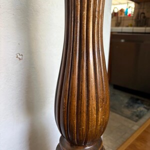 May include: Close-up of a wooden bedpost with a fluted design. The post is a dark brown color and has a carved base.