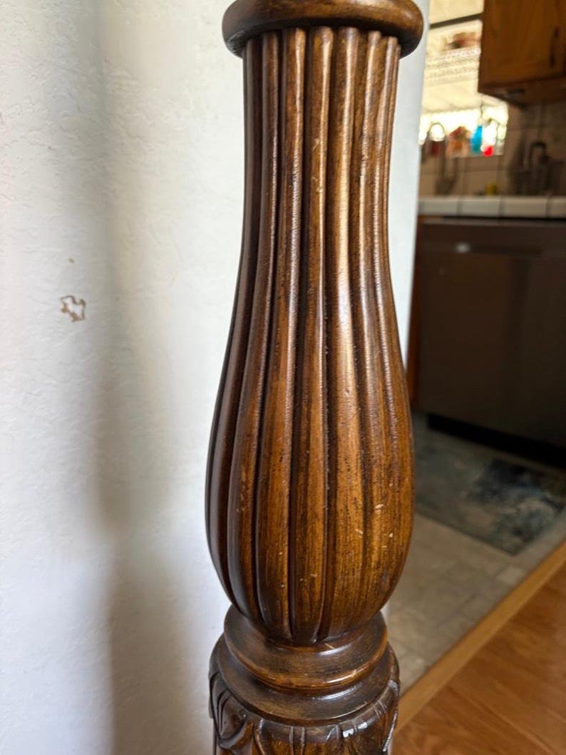 May include: Close-up of a wooden bedpost with a fluted design. The post is a dark brown color and has a carved base.