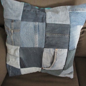 May include: A blue denim pillow with a patchwork design. The pillow is made from different pieces of denim fabric, including pockets and seams. The pillow is sitting on a brown couch.