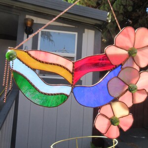 May include: A stained glass mask with a rainbow design and pink flowers. The mask is made of glass and has a copper chain attached to it.