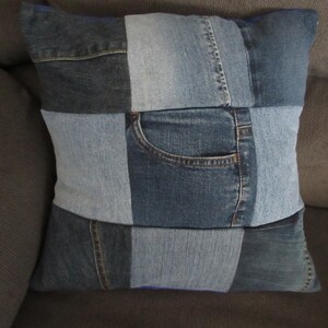 May include: A square pillow cover made from denim fabric. The cover is made of different shades of blue denim and features a patch pocket.