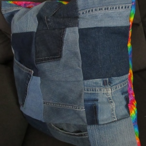 Puede incluir: Una funda de cojín de patchwork hecha de diferentes tonos de mezclilla azul con un borde de arcoíris. La funda de cojín está hecha de materiales reciclados y es una excelente manera de agregar un toque de personalidad a tu hogar.