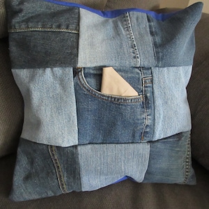 Könnte beinhalten: Ein blaues Jeans-Kissen mit Patchwork-Muster. Das Kissen hat eine große Tasche auf der Vorderseite mit einem beigefarbenen Stofffutter.