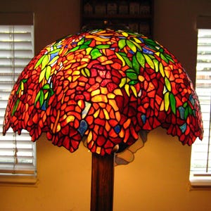 May include: A stained glass lampshade with a floral design in shades of red, orange, yellow, green, and blue. The lampshade is made of many small pieces of glass that are joined together to create a mosaic effect.