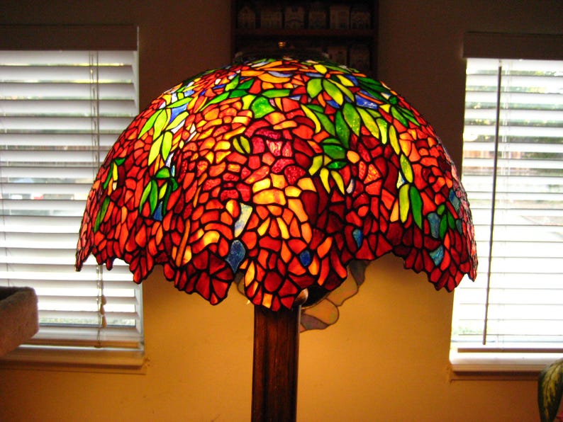 May include: A stained glass lampshade with a floral design in shades of red, orange, yellow, green, and blue. The lampshade is made of many small pieces of glass that are joined together to create a mosaic effect.