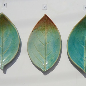 May include: Three ceramic dishes shaped like leaves, labeled 1, 2, and 3. Each dish features a glossy glaze in shades of teal and green with a central vein detail. The middle dish has a reddish-brown tint at the tip, while the others are solid teal.