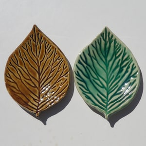 May include: Two ceramic leaf-shaped dishes with a glossy finish. One dish is brown with dark brown veining, and the other is light green with dark green veining. Both items feature a detailed, embossed skeletal leaf pattern on the surface.