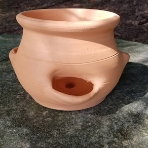 May include: Terracotta planter with a hole in the side, designed for hanging or wall mounting. The planter has a rustic, handmade look and is perfect for adding a touch of nature to any space.