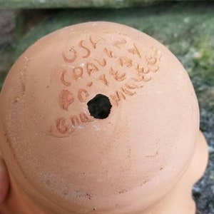 May include: A terracotta-colored ceramic pot with a scalloped edge. The bottom of the pot has the text "USA CRAFTED" and a drainage hole. The pot is likely for planting flowers or herbs.