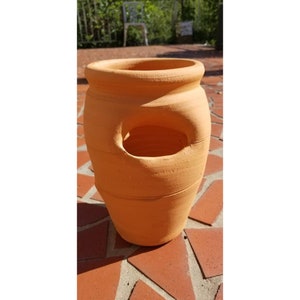 May include: A terracotta planter with a hole in the side. The planter is a light orange color and has a rounded shape.