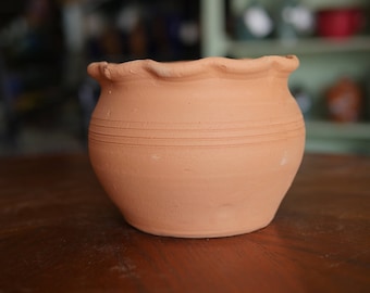May include: A terracotta flower pot with a wavy rim and three horizontal lines around the middle.