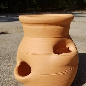 May include: A terracotta planter with multiple holes in the sides. The planter is a light brown color and has a rounded shape.