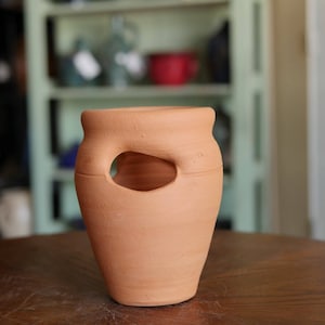 May include: A terracotta planter with a cutout design. The planter is a light brown color and has a smooth, slightly textured surface.