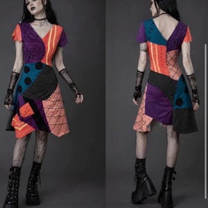 May include: A short-sleeved dress featuring a patchwork design with various patterns and colors including purple, orange, teal, and black. The dress has a V-neckline, a fitted bodice, and a flared skirt with visible stitching details across the panels.
