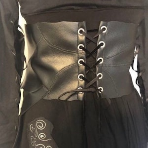 May include: Black faux leather corset with a lace-up back and a black skirt. The corset has a decorative stitching pattern and metal eyelets.