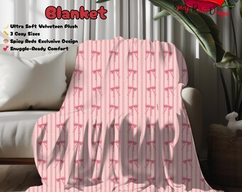 Può includere: Una coperta in velluto rosa con un motivo ripetuto di fiocchi rosa e strisce verticali. La coperta è drappeggiata su un divano bianco. Il testo sulla coperta recita "Velveteen Plush Blanket" e "Ultra Soft Velveteen Plush".