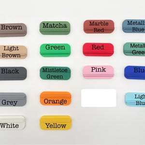 May include: A collection of small, rectangular objects in various colors, each labeled with a corresponding color name in black text. Colors include brown, green, red, blue, and more. The objects have a small, curved handle.