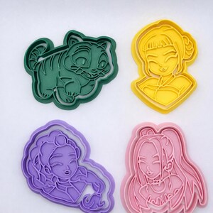 May include: A set of four plastic cookie cutters in various colors. The collection includes a dark green tiger-like creature, a yellow character with a bun hairstyle, a purple character with curly hair, and a pink character with long hair.