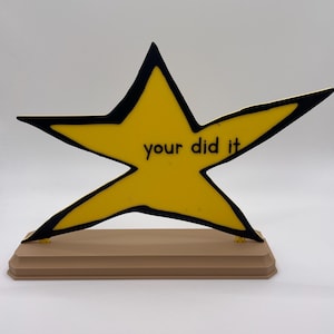 May include: A yellow star-shaped plaque with a thick black outline, mounted on a rectangular tan base. The center of the star features the black text "your did it" printed in a simple, sans-serif font. The object is displayed against a plain background.