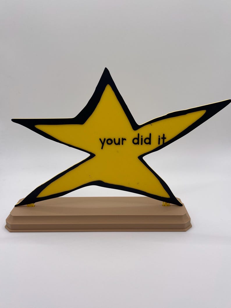 May include: A yellow star-shaped plaque with a thick black outline, mounted on a rectangular tan base. The center of the star features the black text "your did it" printed in a simple, sans-serif font. The object is displayed against a plain background.