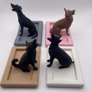 Puede incluir: Cuatro figuras geom&eacute;tricas de perros en negro y marr&oacute;n, cada una sobre una base rectangular en gris, rosa, beige y blanco. Los perros est&aacute;n en varias poses, algunos sentados y otros de pie con la cabeza levantada.