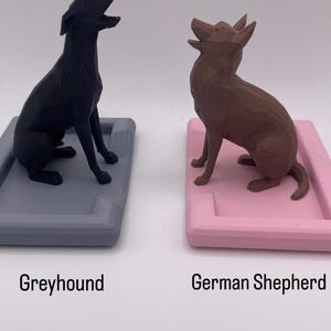Puede incluir: Dos figuras de perros, un galgo negro y un pastor alem&aacute;n marr&oacute;n, est&aacute;n sobre bandejas rectangulares. La bandeja del galgo es gris y la del pastor alem&aacute;n es rosa. Los textos "Greyhound" y "German Shepherd" est&aacute;n debajo.