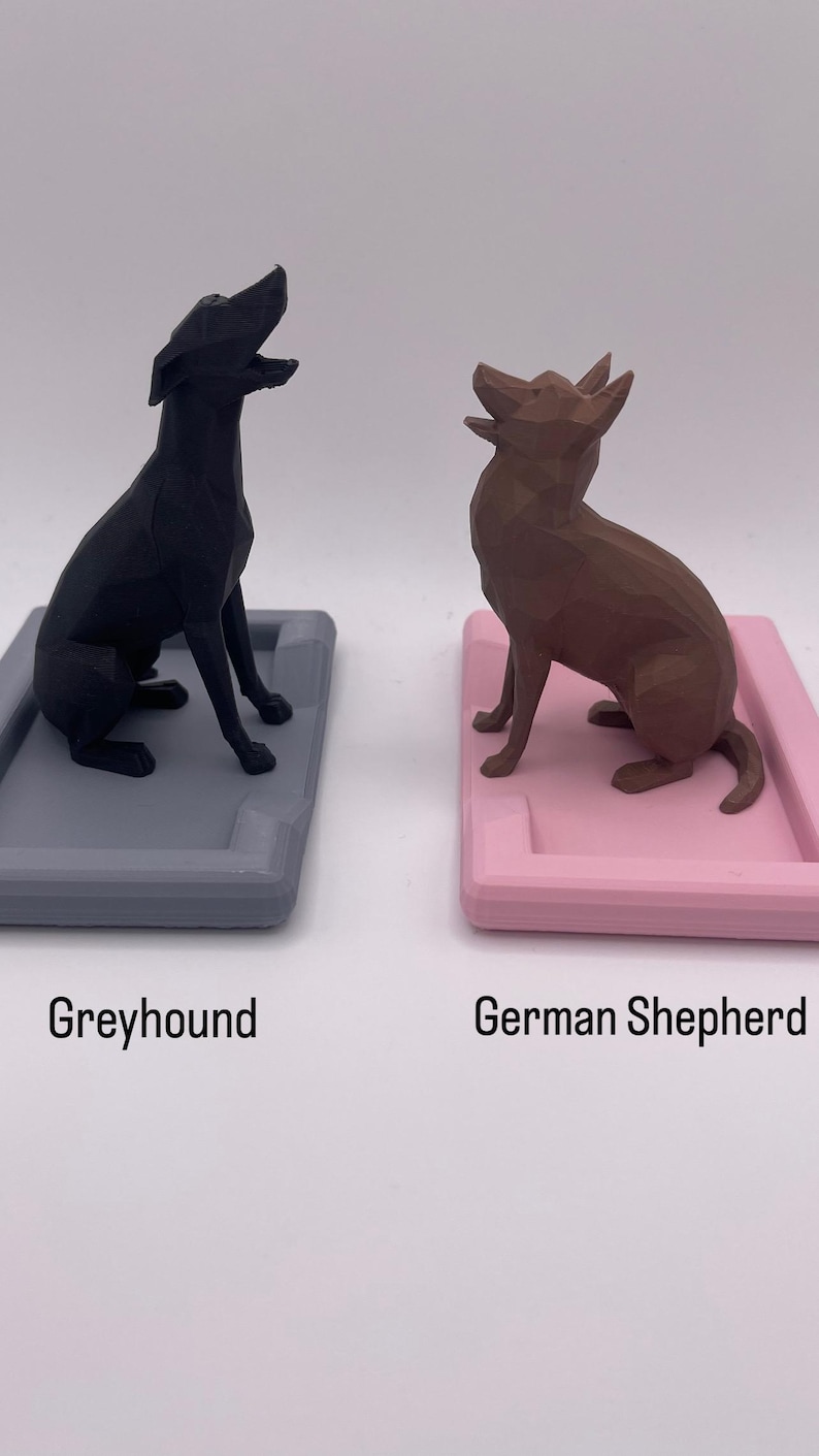 Puede incluir: Dos figuras de perros, un galgo negro y un pastor alem&aacute;n marr&oacute;n, est&aacute;n sobre bandejas rectangulares. La bandeja del galgo es gris y la del pastor alem&aacute;n es rosa. Los textos "Greyhound" y "German Shepherd" est&aacute;n debajo.
