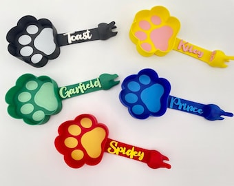 May include: Five colorful paw-shaped pet bowls with handles and personalized names: Toast, Garfield, Riley, Prince, and Spidey. The bowls are made of silicone and are perfect for feeding small pets.