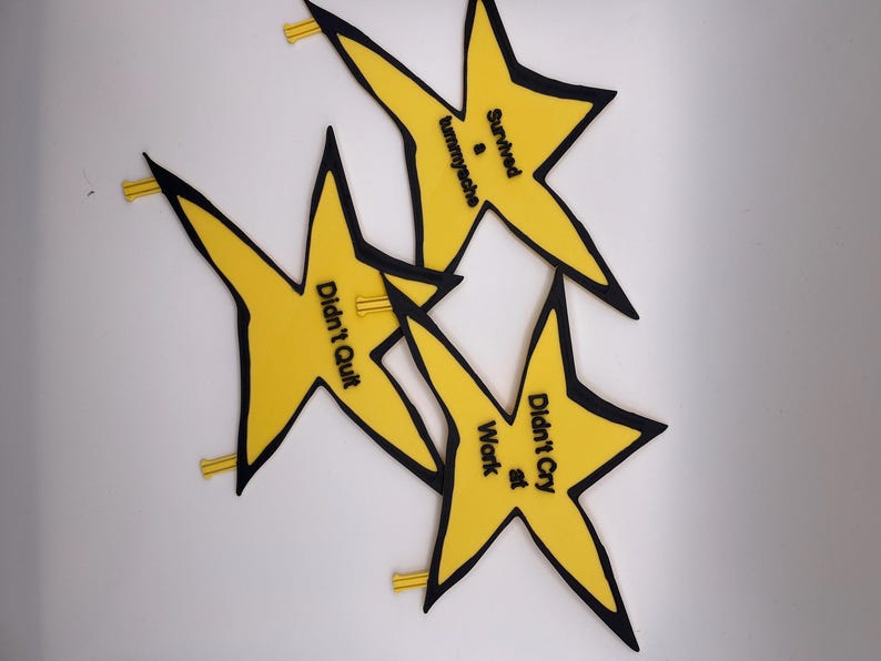 May include: Three yellow star-shaped pins with black outlines. Each star features black text: one reads 'Survived a tummyache', another 'Didn't Quit', and the third 'Didn't Cry at Work'. Each pin has a small yellow backing mechanism visible.