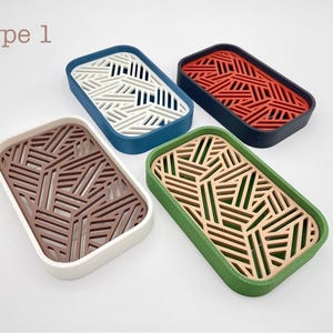 May include: Four rectangular trays with geometric cut-out designs. The trays are in various colors: white and blue, red and black, brown and white, and green and tan. The text "Type 1" is in the upper left corner.