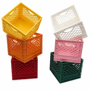 May include: Two stacks of plastic storage crates. The left stack features a yellow crate on top, an orange crate in the middle, and a red crate at the base. The right stack features a white crate on top, a pink crate in the middle, and a dark green crate at the base. Each crate has a diamond-patterned grid design and integrated handles.