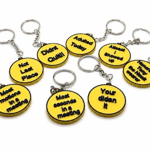 May include: A collection of yellow and black keychains with various phrases. The keychains have a circular design with black text on a yellow background. Phrases include "Adulted Today" and "Didn't Quit!!". Each keychain has a silver keyring.