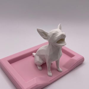 Puede incluir: Una figura geom&eacute;trica blanca de Chihuahua con la boca abierta est&aacute; sobre una bandeja rectangular rosa. La palabra "Chihuahua" est&aacute; impresa en negro en la parte inferior de la bandeja. El fondo es blanco liso.