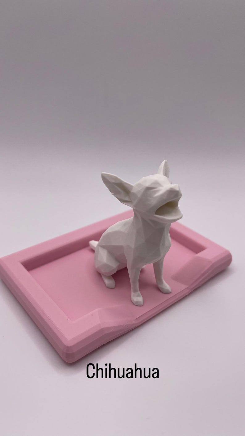 Puede incluir: Una figura geom&eacute;trica blanca de Chihuahua con la boca abierta est&aacute; sobre una bandeja rectangular rosa. La palabra "Chihuahua" est&aacute; impresa en negro en la parte inferior de la bandeja. El fondo es blanco liso.