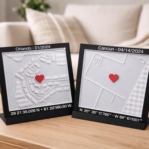 May include: Two black framed map art pieces, one labeled "Orlando - 01/2024" and the other "Cancun - 04/14/2024". Each features a white map with a red heart marking a location. Coordinates are listed below each map.
