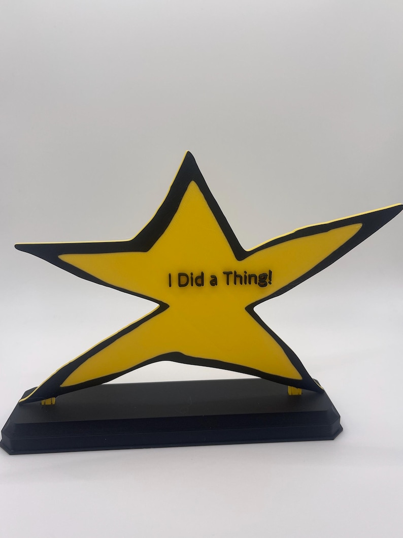 May include: A yellow star-shaped award with a black outline, mounted on a rectangular black base. The center of the star features the black text "I Did a Thing!" in a sans-serif font. The design is flat and graphic with bold, clean lines.