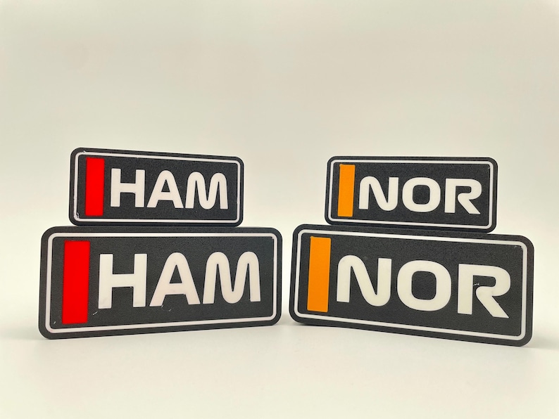 以下が含まれることがあります： 白文字の黒い長方形のラベルが2組。上のラベルは「HAM」と「NOR」で、それぞれ赤とオレンジのストライプが入っている。下のラベルは「HAM」と「NOR」で、それぞれ赤とオレンジのストライプが入っている。