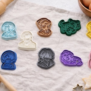 May include: A collection of nine plastic cookie cutters in various colors including light blue, white, brown, dark green, yellow, dark blue, gray, purple, and pink. Each cutter features a detailed embossed design of a different character portrait.