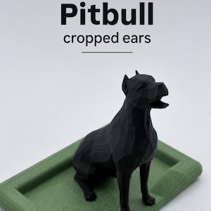 Puede incluir: Escultura negra de un perro Pitbull con orejas cortadas, de estilo geom&eacute;trico, sobre una base rectangular verde. El texto "Pitbull cropped ears" est&aacute; encima. Dise&ntilde;o moderno y angular.