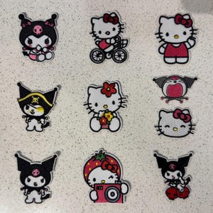 May include: A collection of nine embroidered patches featuring Sanrio characters including Hello Kitty and Kuromi. The designs include Hello Kitty on a bicycle, holding flowers, wearing a strawberry hat with a camera, and various Kuromi poses.