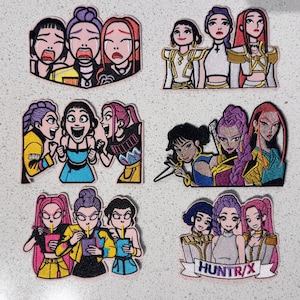 May include: Six embroidered patches featuring groups of three animated characters in various poses and outfits. The designs include crying, cheering, and eating figures, with one patch displaying the text HUNTR/X on a white banner at the bottom.