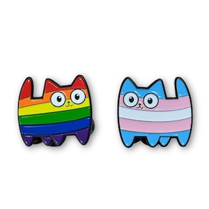 May include: Two enamel pins in the shape of cartoon cats. One cat is colored with the rainbow flag, the other with the transgender flag. Both have large, round eyes and small smiles. The pins are on a white background.