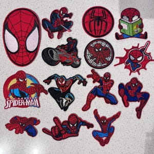 May include: A collection of thirteen embroidered fabric patches featuring Spider-Man in various poses, including a large mask, a character on a motorcycle, a character reading a book, and the text "The Amazing Spider-Man" on a circular patch.