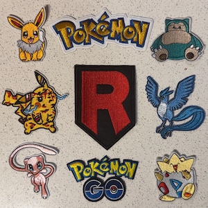 May include: A selection of embroidered Pokémon patches, showcasing characters like Eevee, Pikachu, Snorlax, Articuno, Mew, and Togepi. Also includes a Team Rocket patch and Pokémon and Pokémon GO logos. The patches are brightly coloured and intricately designed.