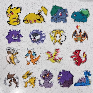 May include: A collection of sixteen embroidered patches featuring various colourful cartoon creatures, including yellow electric types, blue plant-based beings, purple ghosts, orange dragons, a fiery bird, a red lizard, a brown insect, and a blue sea creature.