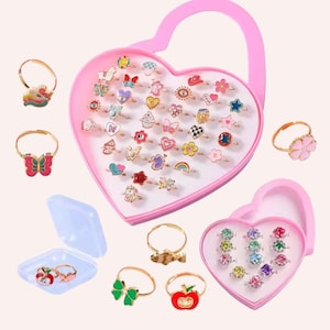May include: A collection of colorful children's rings in a pink heart-shaped case. The rings feature various designs, including butterflies, flowers, hearts, and stars. Some rings are displayed outside the case, showcasing the variety of styles and colors.