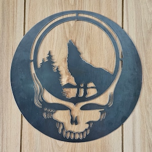 May include: A circular metal wall art piece featuring a howling wolf silhouette within a circle, set against a forest and skull design. The artwork is in a dark, metallic finish, mounted on a wooden background.