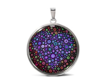Könnte beinhalten: Eine silberne Halskette mit einem runden Anhänger, der mit einem farbenfrohen Mandala-Design verziert ist. Das Mandala zeigt eine Vielzahl von Farbtönen in Lila, Blau, Grün und Rot.