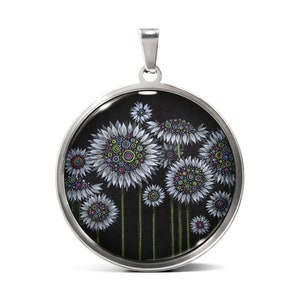 Puede incluir: Un collar con un colgante redondo de plata, sobre fondo negro, adornado con flores blancas con centros coloridos.