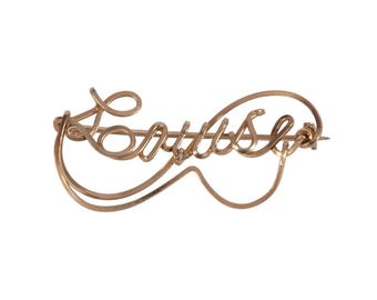 May include: A gold-toned brooch with the word "Louise" written in cursive.